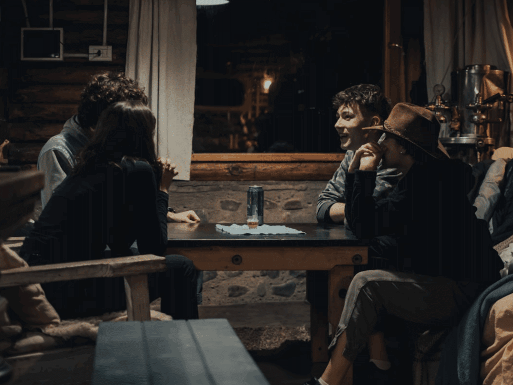 Group of friends sitting around a table, engaged in conversation in a cozy, dimly lit room.